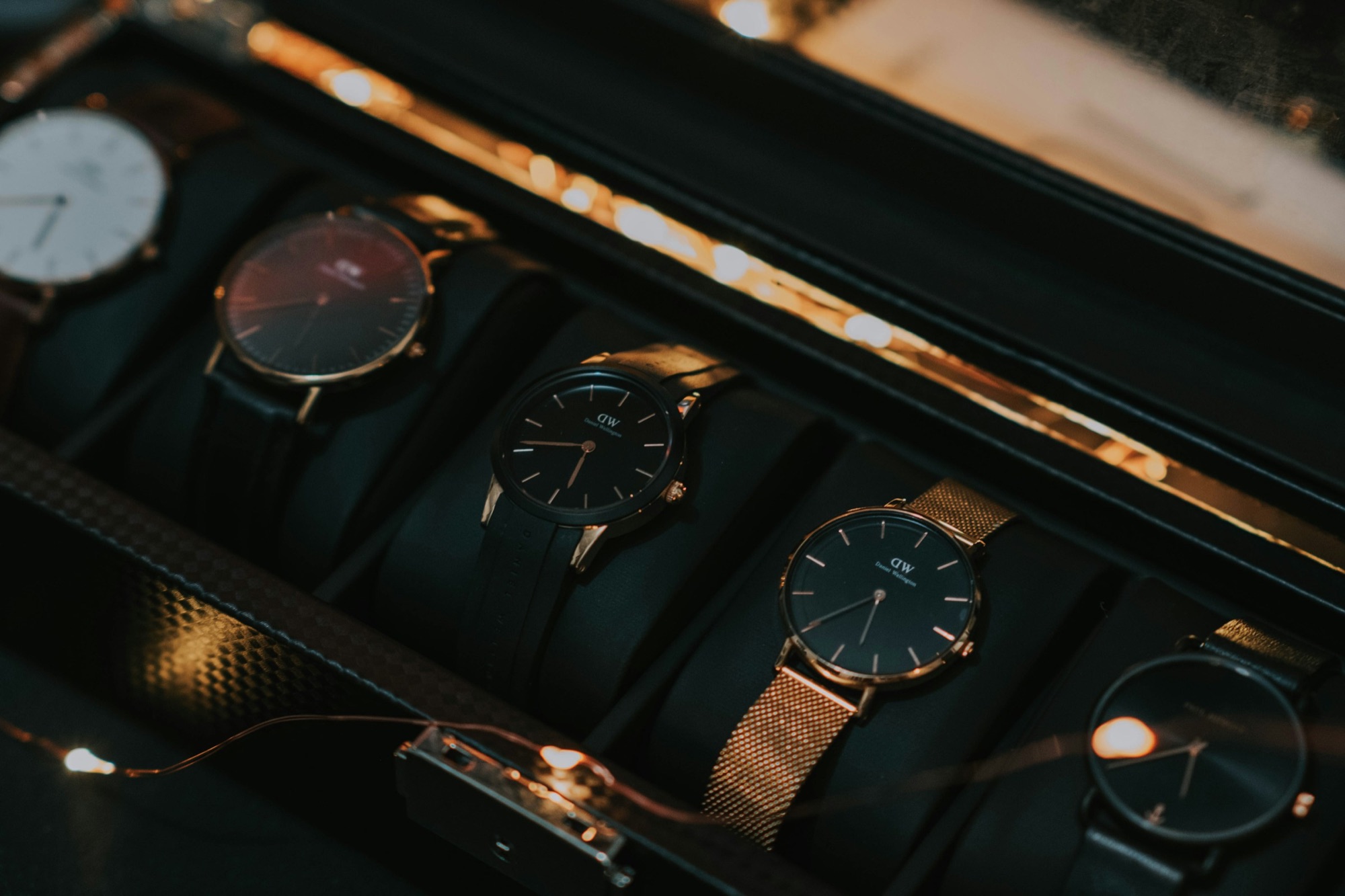 Several watches resting in the lined slots of a dark watch box under warm light