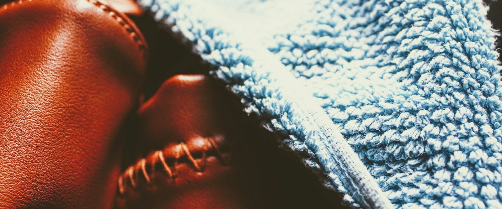 A blue microfiber cloth draped over rich brown stitched leather, close up
