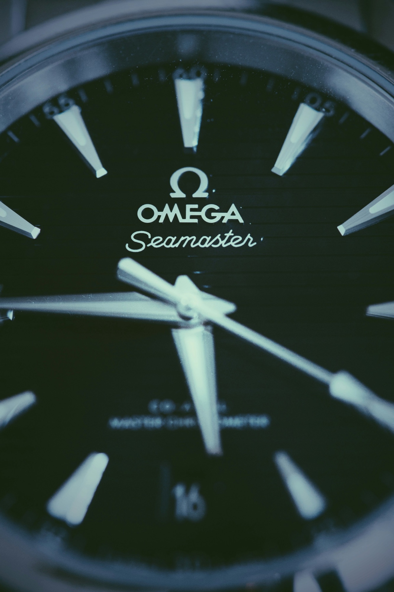 An extreme close up of a black dive watch dial and applied hour markers